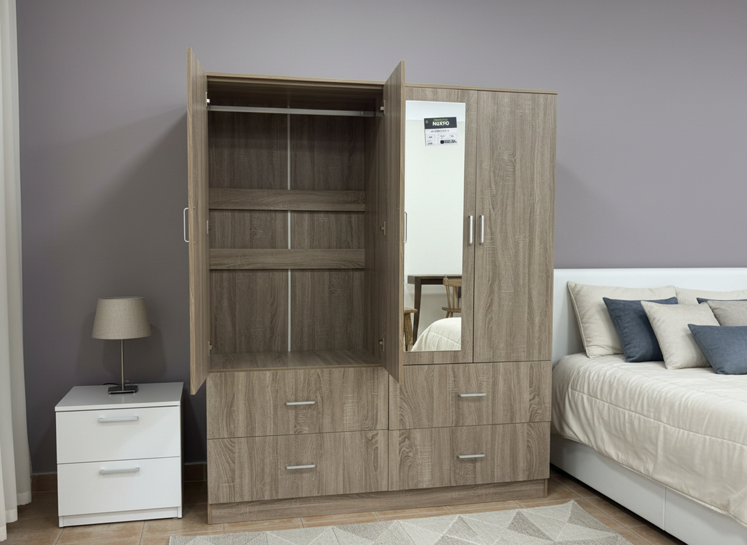 Armario de madera con puertas abiertas que dejan ver los estantes, junto a una mesita de noche blanca con una lámpara. Cerca, una cama con cojines blancos y azules. Un dormitorio acogedor.