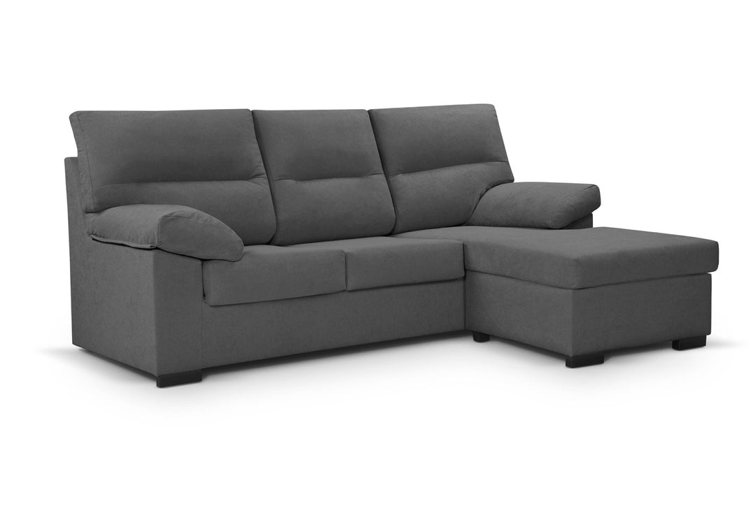 Un moderno sofá modular gris con mullidos cojines y una chaise longue a la derecha. La tela es suave, lo que crea un ambiente acogedor y agradable.