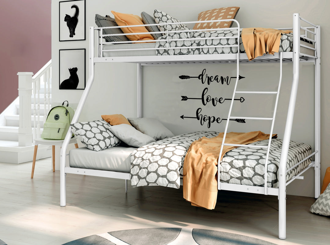 Un dormitorio elegante con una litera de metal blanco. La ropa de cama presenta motivos geométricos en gris y blanco, realzados con mantas naranjas. En la pared, unas letras de vinilo forman las palabras «sueño», «amor» y «esperanza», con flechas que apuntan hacia los lados. Una mochila verde cuelga de una silla, junto a un cuadro de un gato en la pared, creando un ambiente moderno y acogedor.