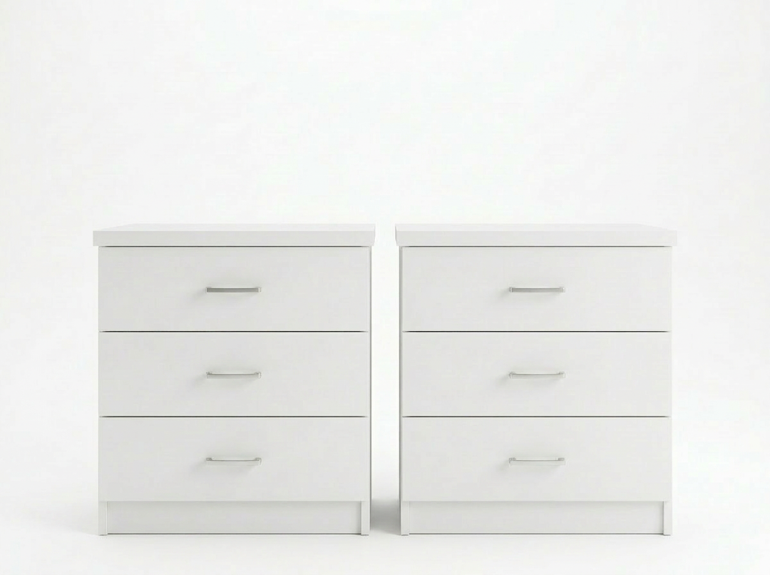 Dos cómodas blancas idénticas de tres cajones, con elegantes tiradores plateados, se alzan una junto a otra sobre un fondo blanco liso, transmitiendo una estética minimalista y moderna.