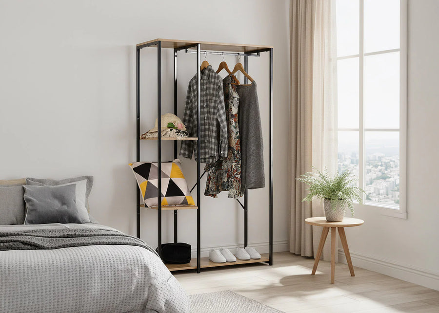 Dormitorio minimalista con la cama perfectamente hecha, un armario abierto con ropa, cojines geométricos y una planta en una maceta sobre una mesita junto a un gran ventanal.