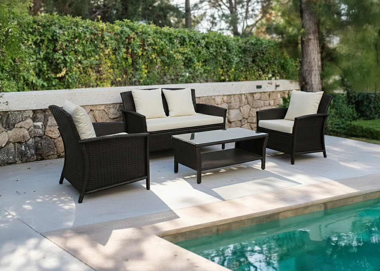 Conjunto de muebles de exterior junto a una piscina, compuesto por muebles de mimbre oscuro con cojines de color beige. Rodeado de vegetación y un muro de piedra, lo que crea un ambiente sereno.