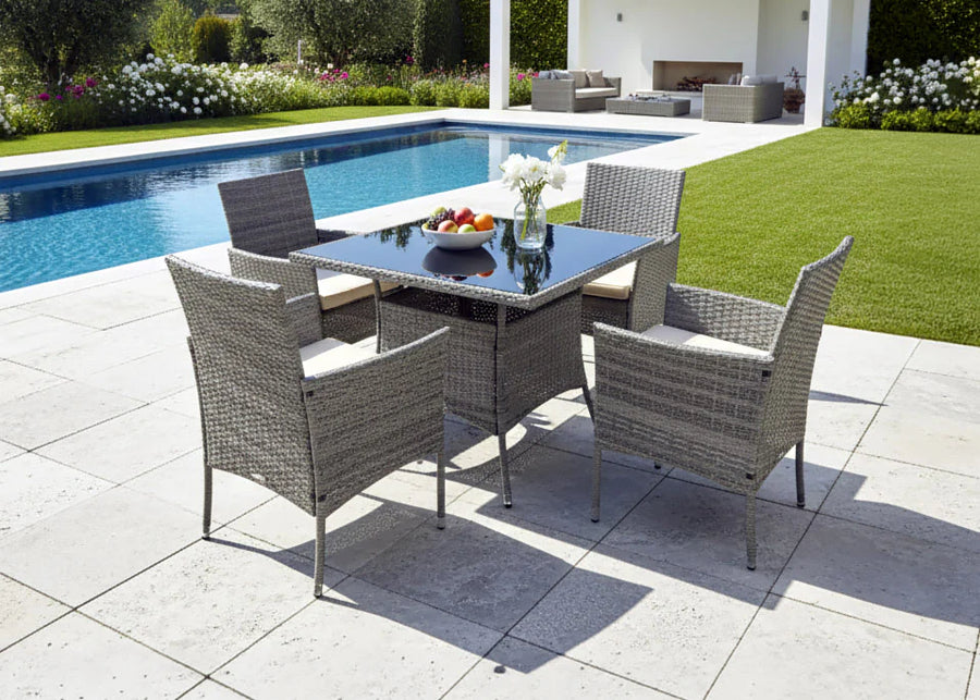 Un patio al aire libre con un conjunto de comedor de mimbre junto a una elegante piscina. Un cuenco con fruta y un jarrón con flores decoran la mesa, rodeada de una exuberante vegetación y una acogedora zona de descanso, lo que crea un ambiente sereno y acogedor.