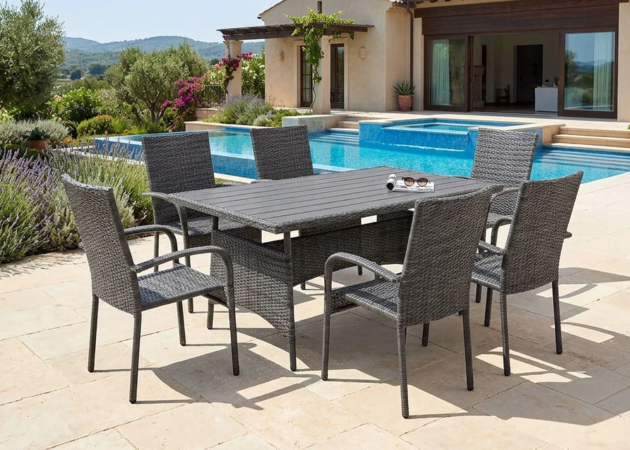 Patio al aire libre con un conjunto de comedor de mimbre para seis personas junto a una piscina de color turquesa. Al fondo, una villa de estilo mediterráneo rodeada de una exuberante vegetación.