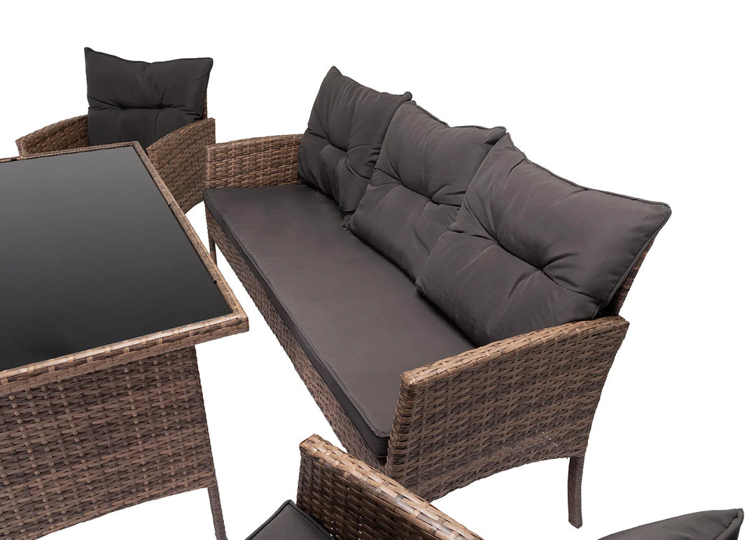 Conjunto de muebles de exterior con diseño de mimbre, compuesto por una mesa con tablero de cristal y asientos acolchados de color gris oscuro, que crean un ambiente acogedor y agradable.