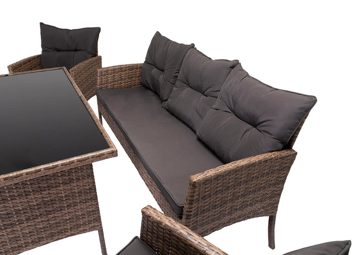Conjunto de muebles de exterior con diseño de mimbre, compuesto por una mesa con tablero de cristal y asientos acolchados de color gris oscuro, que crean un ambiente acogedor y agradable.