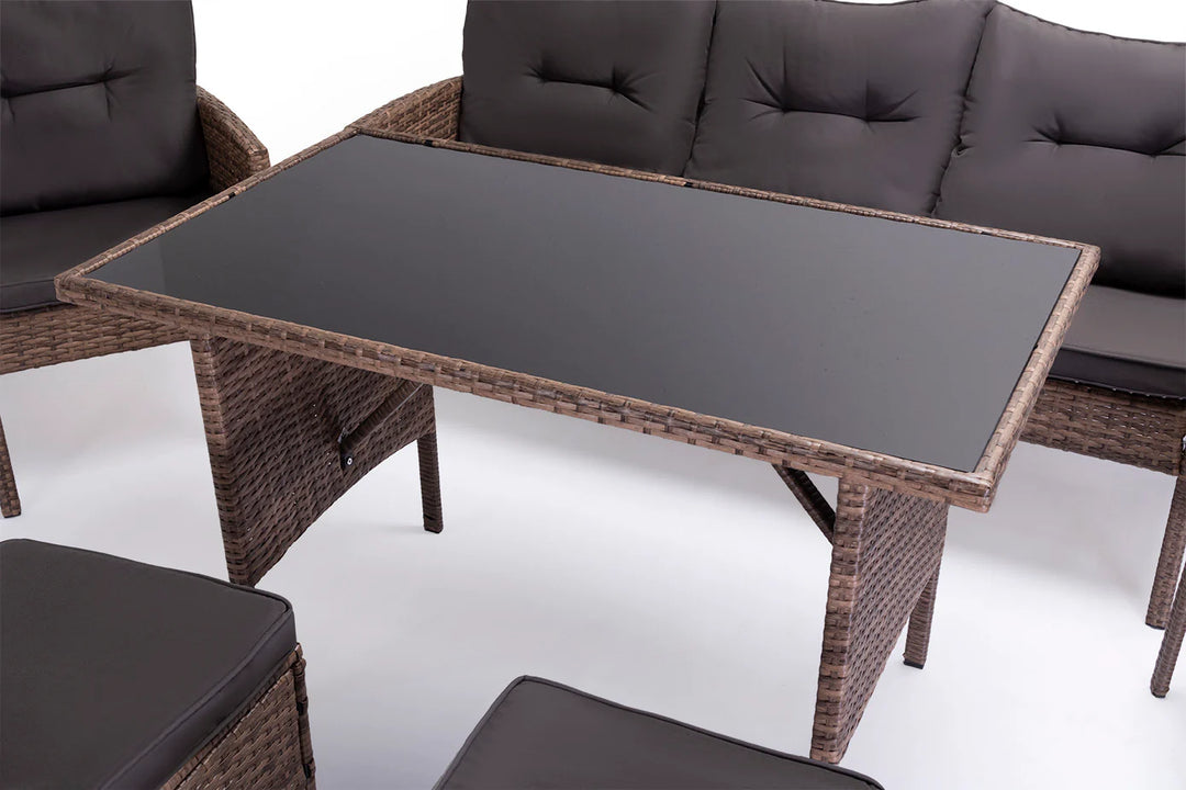 Conjunto de muebles de exterior con diseño de mimbre, compuesto por una mesa con tablero de cristal y asientos acolchados de color gris oscuro, que crean un ambiente acogedor y agradable.