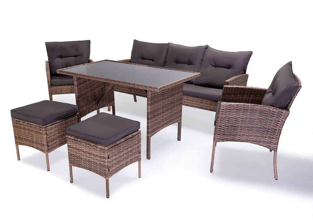 Conjunto de muebles de exterior de ratán compuesto por una mesa con tablero de cristal, un sofá con cojines, dos sillones y dos taburetes. El mimbre marrón, combinado con cojines oscuros, transmite una gran sensación de comodidad.