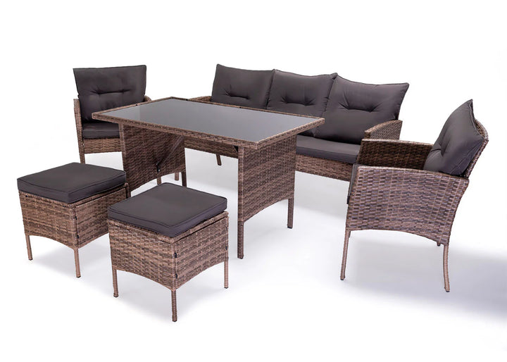 Conjunto de muebles de exterior de ratán compuesto por una mesa con tablero de cristal, un sofá con cojines, dos sillones y dos taburetes. El mimbre marrón, combinado con cojines oscuros, transmite una gran sensación de comodidad.