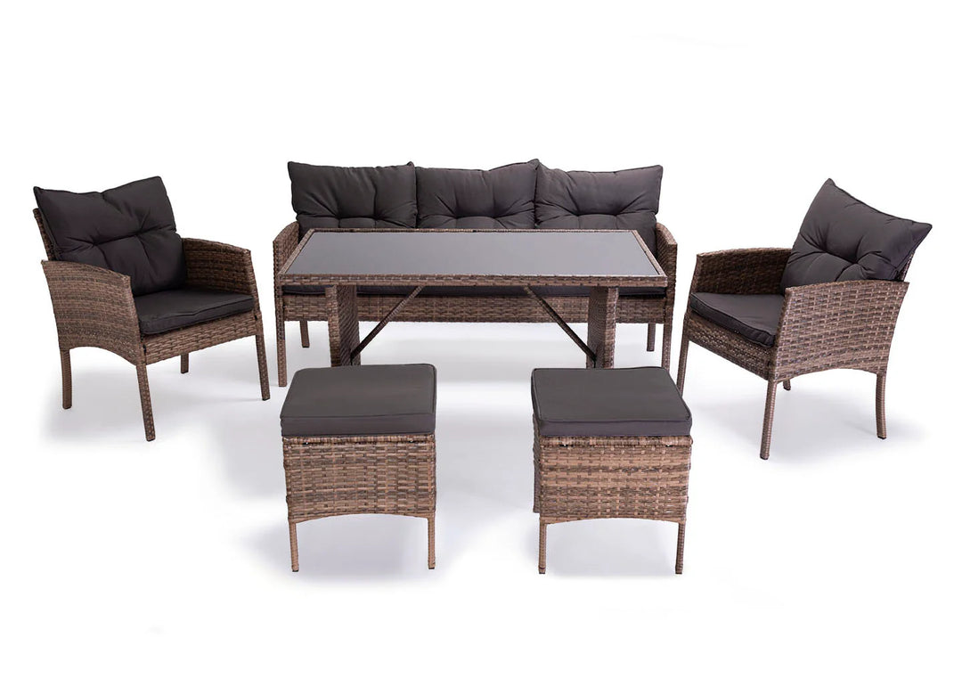 Conjunto de muebles de exterior de ratán marrón compuesto por una mesa con tablero de cristal, un sofá, dos sillones y dos taburetes acolchados. Los cojines son de color gris oscuro.