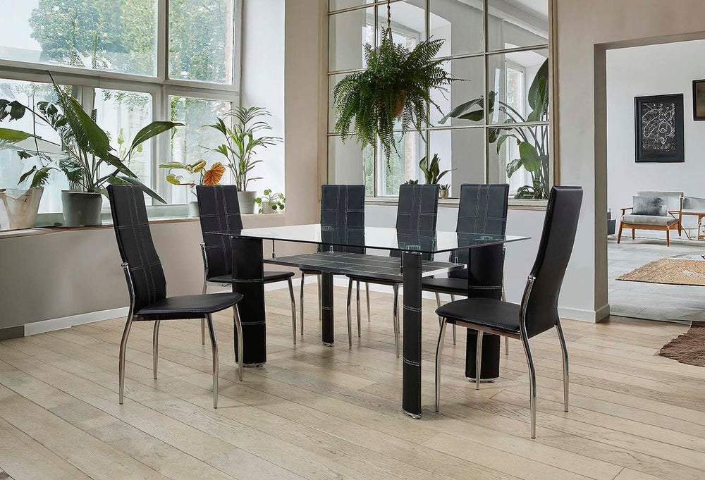 Comedor moderno con una mesa de cristal y seis sillas de cuero negro sobre un suelo de madera clara. Los grandes ventanales y las plantas verdes crean un ambiente fresco y diáfano.