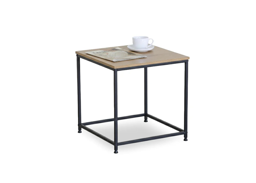 Mesita auxiliar cuadrada de madera con patas de metal negro. Sobre ella descansan una taza y un platillo blancos y un periódico doblado, lo que sugiere un ambiente minimalista e informal.