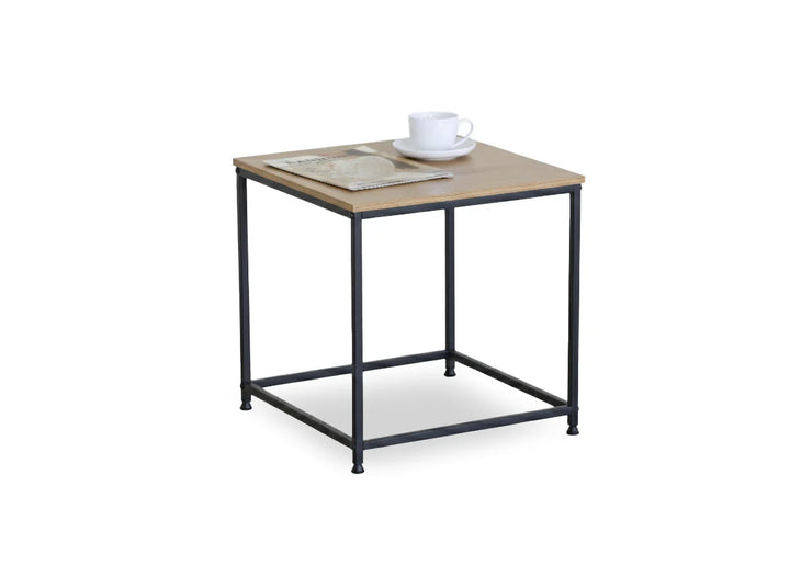 Mesita auxiliar cuadrada de madera con patas de metal negro. Sobre ella descansan una taza y un platillo blancos y un periódico doblado, lo que sugiere un ambiente minimalista e informal.
