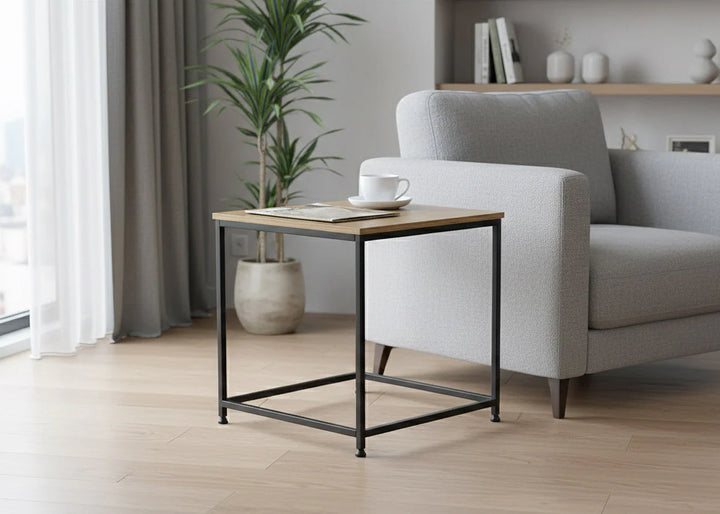 Salón moderno con un sillón gris claro junto a una mesa minimalista sobre la que hay una taza de café. Una planta en maceta y unas estanterías aportan un toque acogedor.