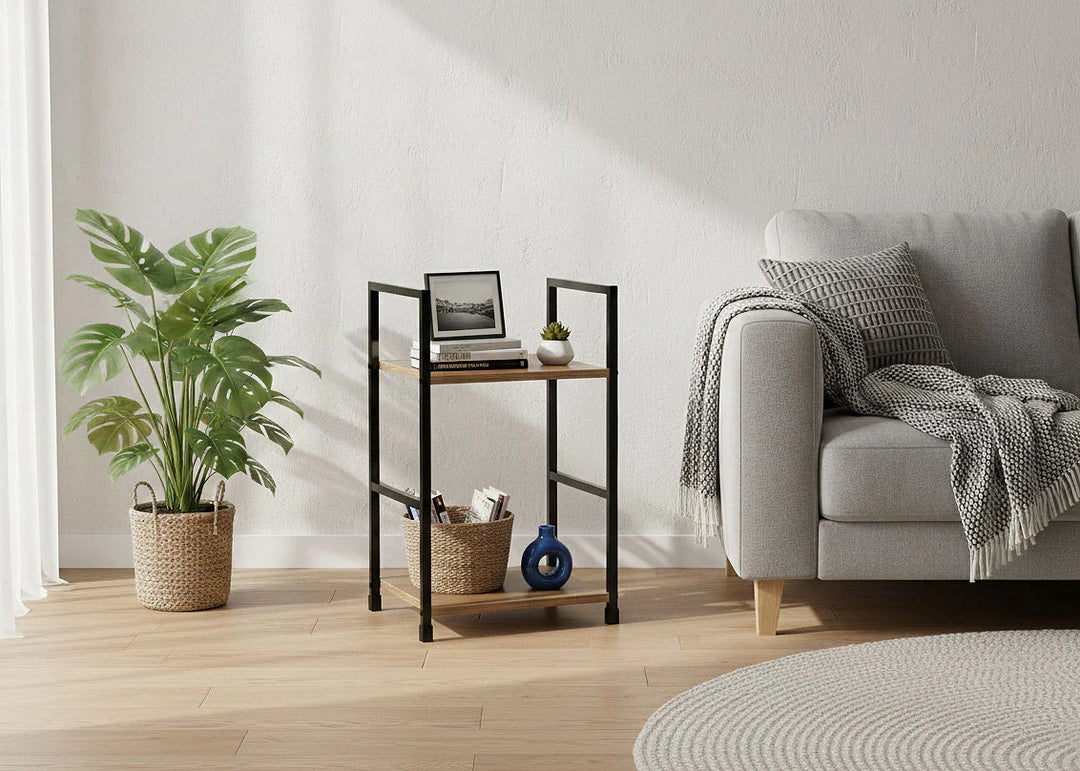 Salón moderno con un sofá gris, cojines estampados y una manta acogedora. Junto a una planta frondosa en una cesta de mimbre hay una mesita con objetos decorativos. Ambiente suave y sereno.