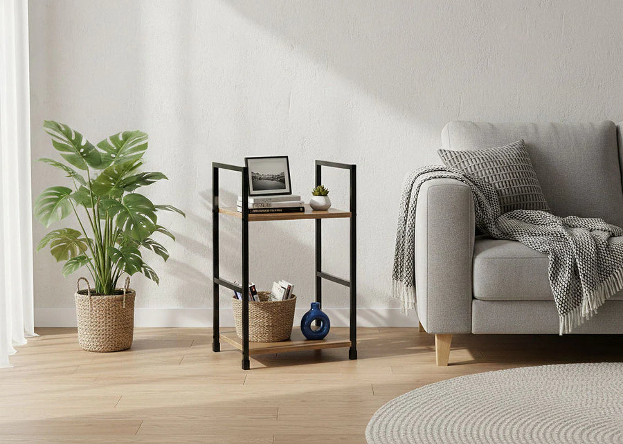 Salón moderno con un sofá gris, cojines estampados y una manta acogedora. Junto a una planta frondosa en una cesta de mimbre hay una mesita con objetos decorativos. Ambiente suave y sereno.