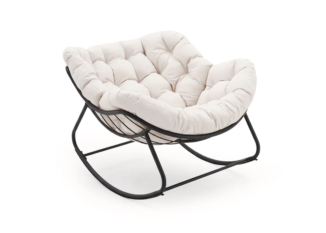 Cómoda mecedora de color crema con mullidos cojines capitoné. La silla cuenta con un asiento profundo y una elegante estructura de metal negro que se curva suavemente.