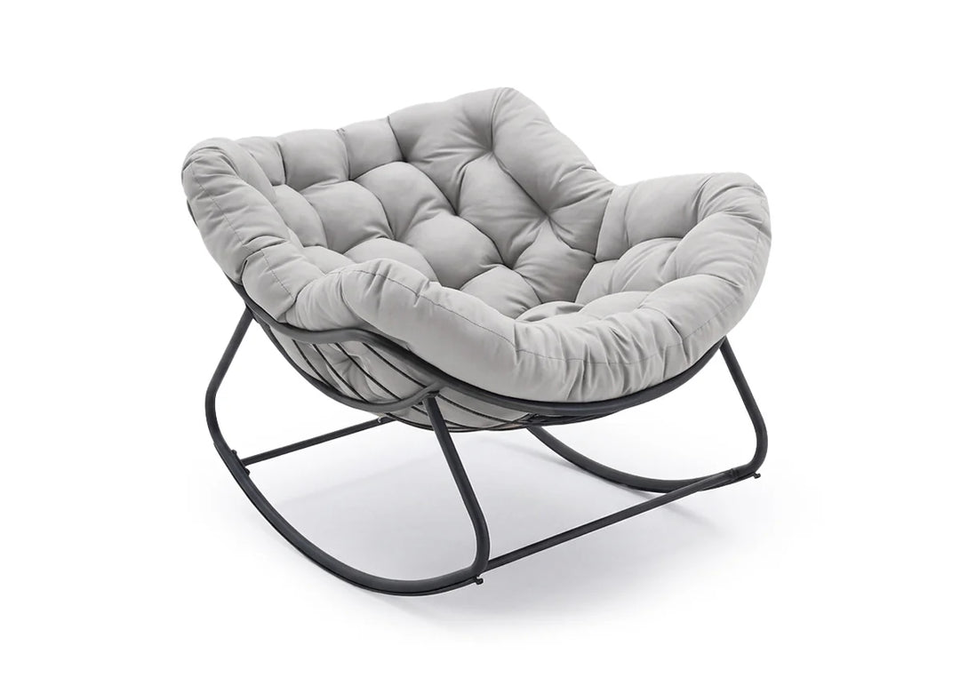 Una lujosa silla acolchada de color gris, con diseño capitoné, sobre una estructura oscilante de metal negro. La silla transmite comodidad y elegancia moderna.