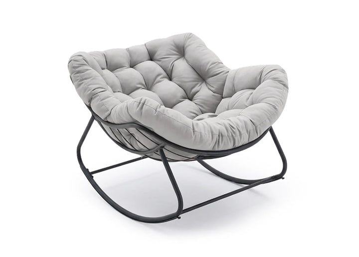 Una lujosa silla acolchada de color gris, con diseño capitoné, sobre una estructura oscilante de metal negro. La silla transmite comodidad y elegancia moderna.