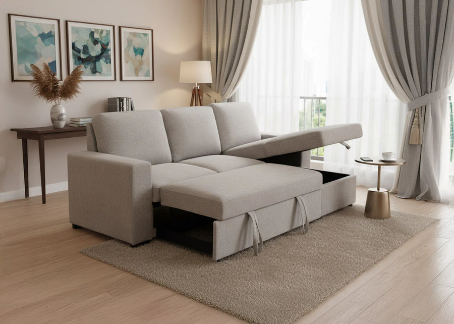 Un salón moderno con un sofá modular de color beige que cuenta con espacio de almacenamiento abierto. Se encuentra sobre una alfombra clara, junto a una ventana con cortinas ligeras. Los cuadros de la pared y una lámpara de mesa completan la decoración.