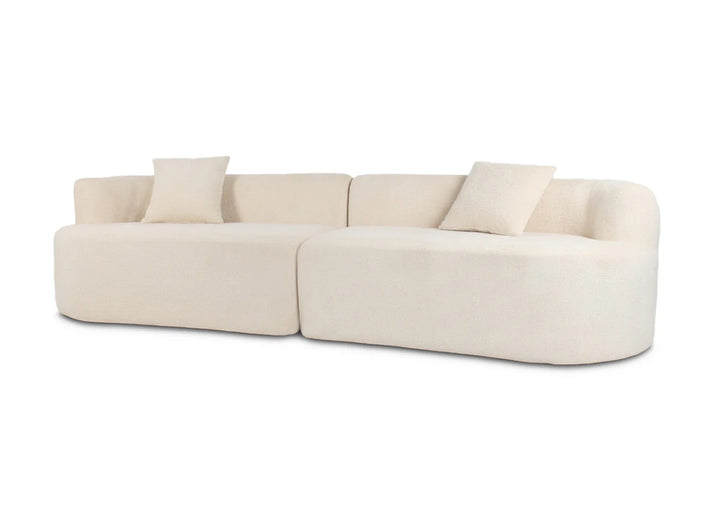Sofá de color beige adornado con varios cojines, con fondo blanco.