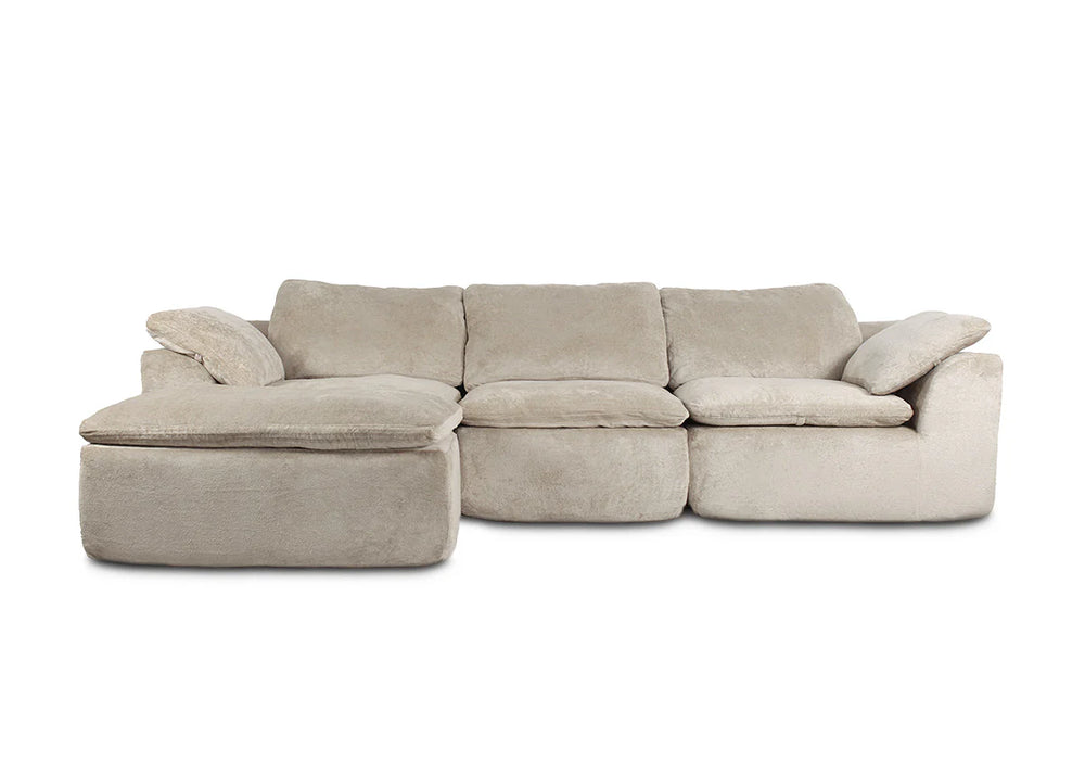 Un lujoso sofá modular de color beige que transmite una sensación acogedora y agradable. Cuenta con asientos y respaldos acolchados, y una chaise longue en el lado izquierdo, todo ello sobre un fondo blanco liso.