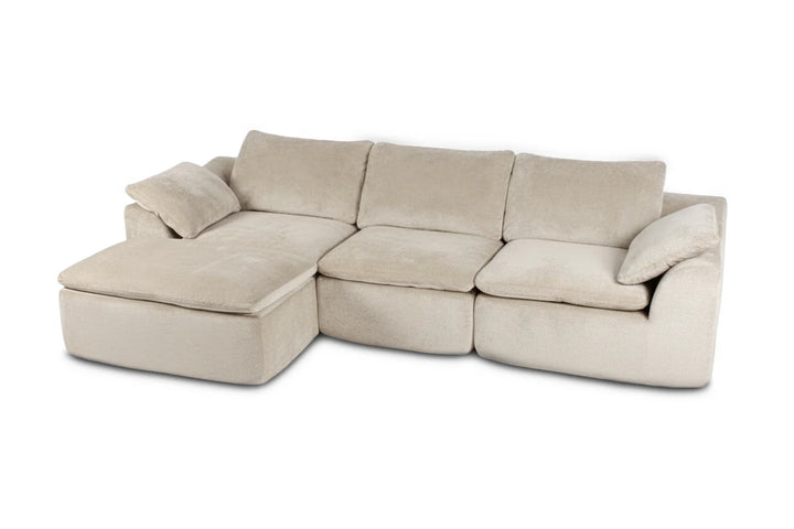 Sofá modular de color beige claro con mullidos cojines, que cuenta con una chaise longue en el lado izquierdo. Transmite un ambiente acogedor y agradable.