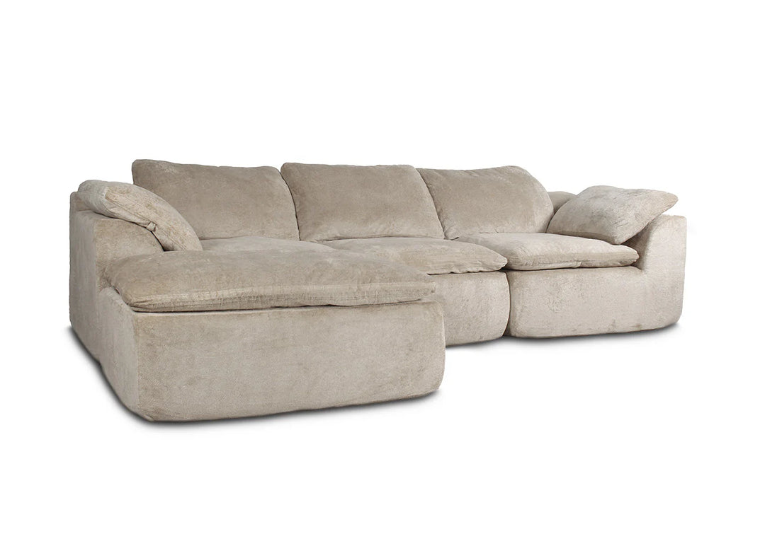 Sofá modular de color beige con mullidos cojines y chaise longue, sobre un fondo blanco. Transmite comodidad y relajación, ideal para un salón acogedor.