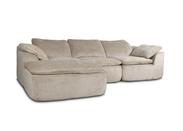 Sofá modular de color beige con mullidos cojines y chaise longue, sobre un fondo blanco. Transmite comodidad y relajación, ideal para un salón acogedor.