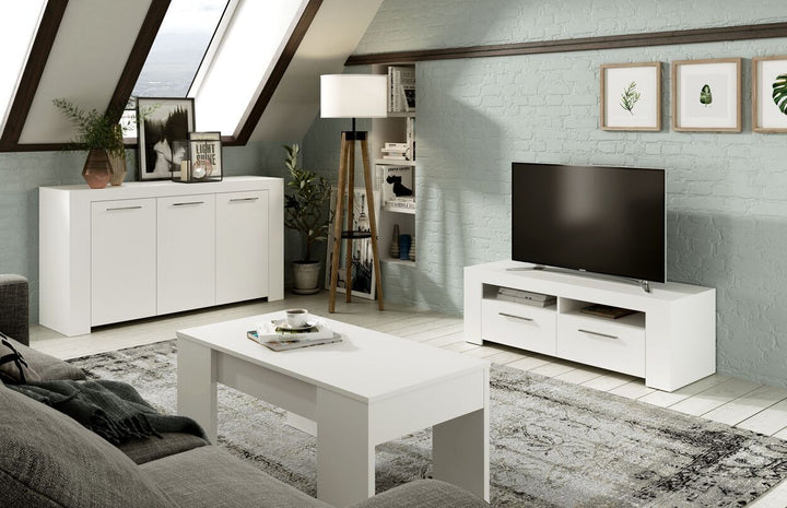 Salón moderno con muebles blancos, entre los que se incluyen un mueble para la televisión y una mesa de centro. Las claraboyas iluminan la estancia, mientras que las plantas y los cuadros aportan un toque acogedor.