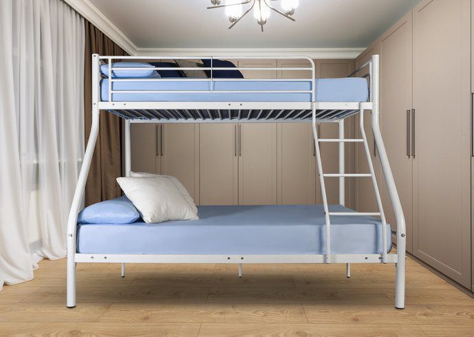 Literas con sábanas azul claro en una habitación con armarios de color beige, suelos de madera y una cortina a la izquierda. Una lámpara de techo le da un toque de elegancia.